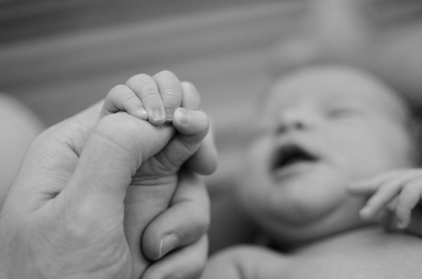 A black and white picture of a baby holding an adults hand