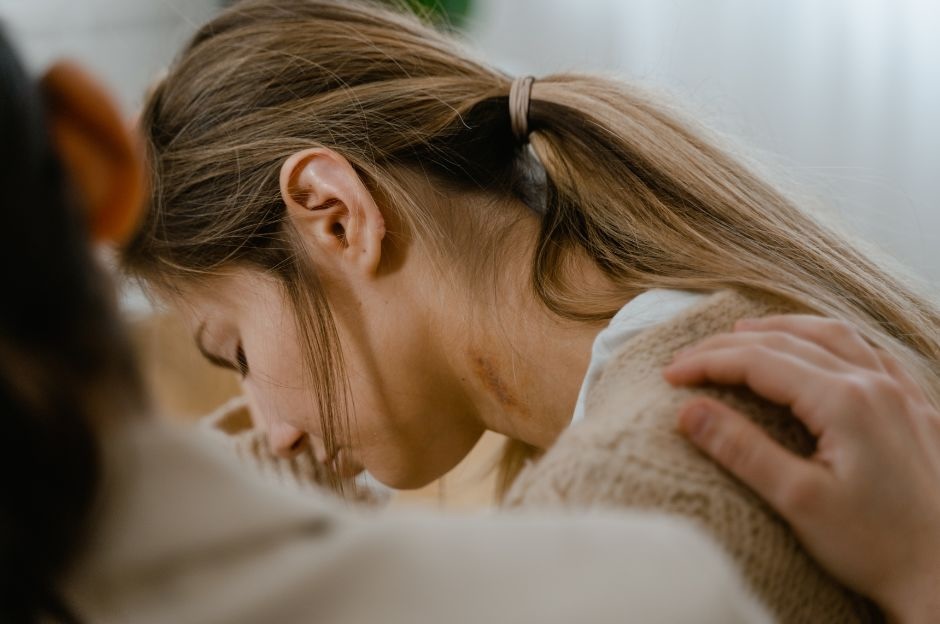 A girl holding her head sadly while another woman holds her shoulder compassionately
